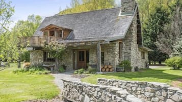 Una casa de piedra con techo inclinado, una terraza de madera y un camino de piedra que lleva a la entrada.