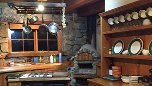 A rustic kitchen with wooden cabinets, a stone wall, and a wood-fired oven. - Galaxy Lounge (Burkes Pass)
