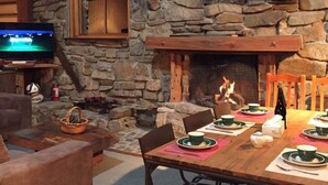 A cozy stone-floored living room with a fireplace, a television, and a dining area set for a meal. - Galaxy Lounge (Burkes Pass)