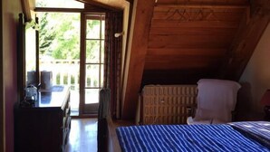 A room with a sloped ceiling, a bed with a blue and white striped bedspread, a chair, and a small table with items on it. - Galaxy Lounge (Burkes Pass)