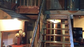 A wooden staircase with a metal railing leading to a second-floor balcony. A wooden desk with a vase of dried flowers is visible on the first floor. - Galaxy Lounge (Burkes Pass)