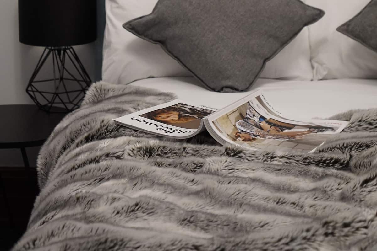 A neatly made bed with a tufted headboard, two pillows, and a magazine on the bed.
