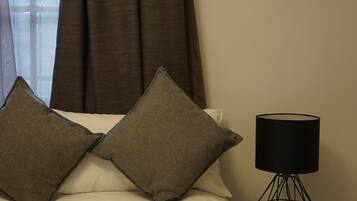 A neatly made bed with two pillows, a black lamp on a side table, and a window with curtains.