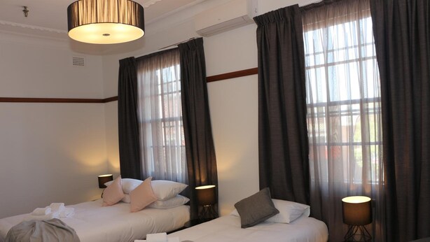A hotel room with two beds, a standing lamp, and a large window with curtains. - Guildford Hotel (Guildford)
