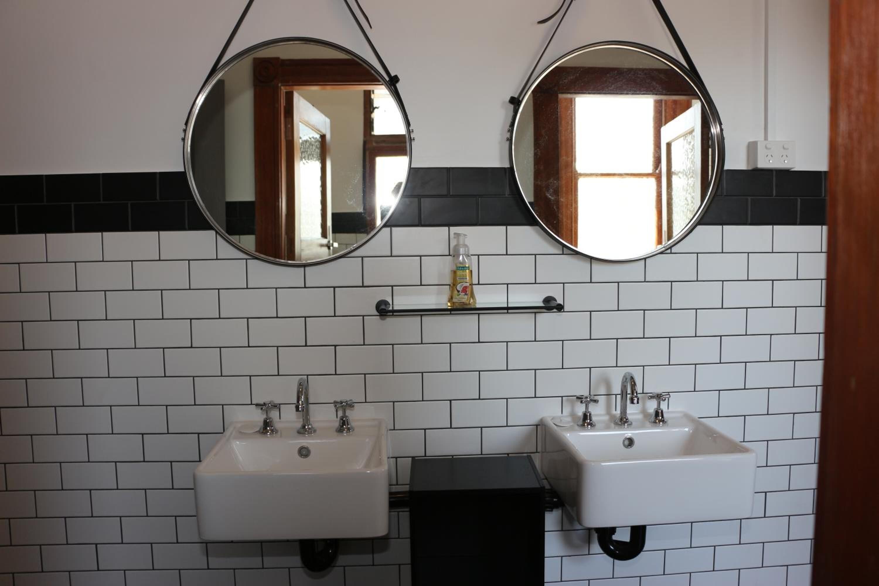 A bathroom with two sinks, two round mirrors, and a shelf with toiletries.