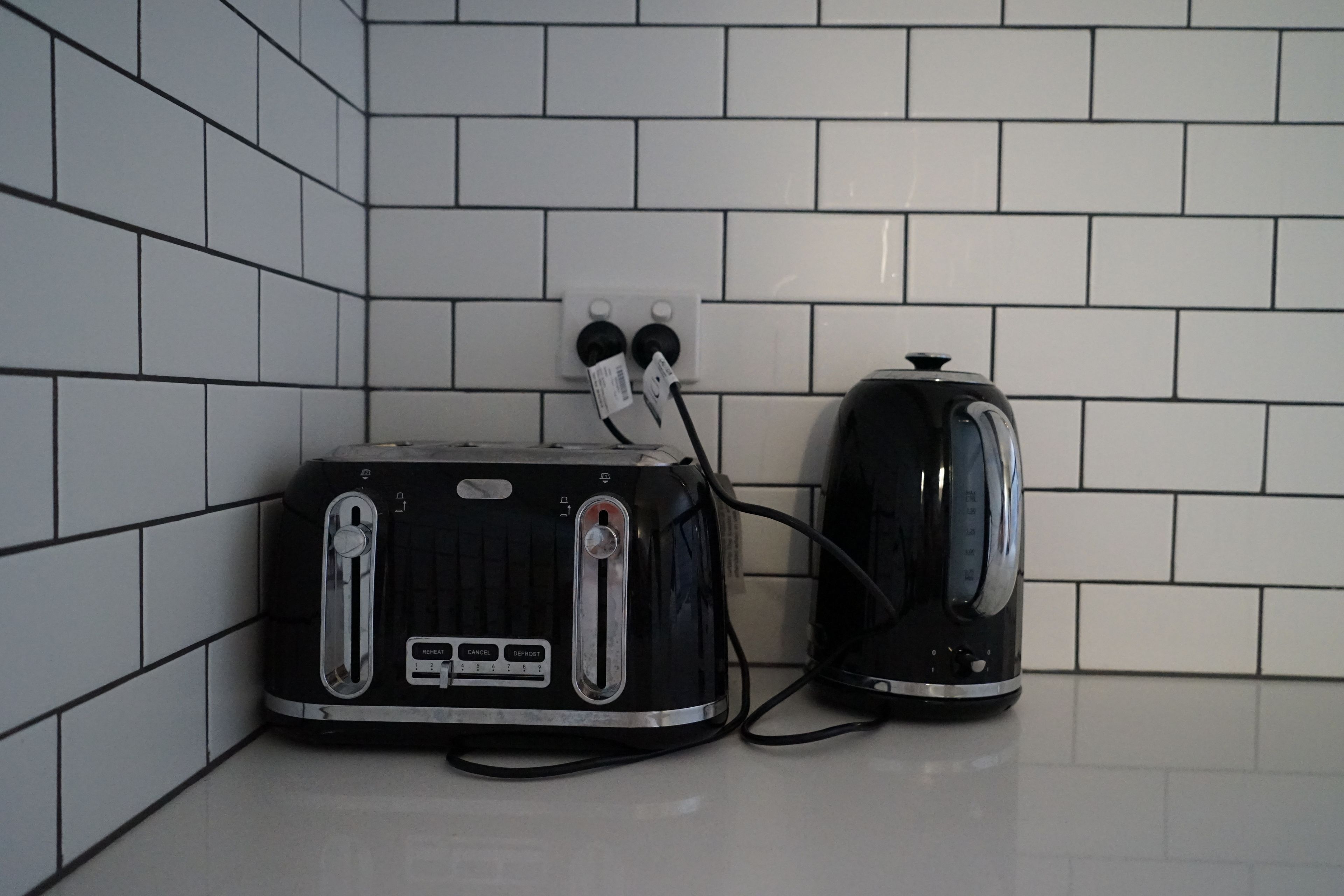 Una cocina con paredes de azulejos blancos y un tostador y hervidor negros sobre la encimera.