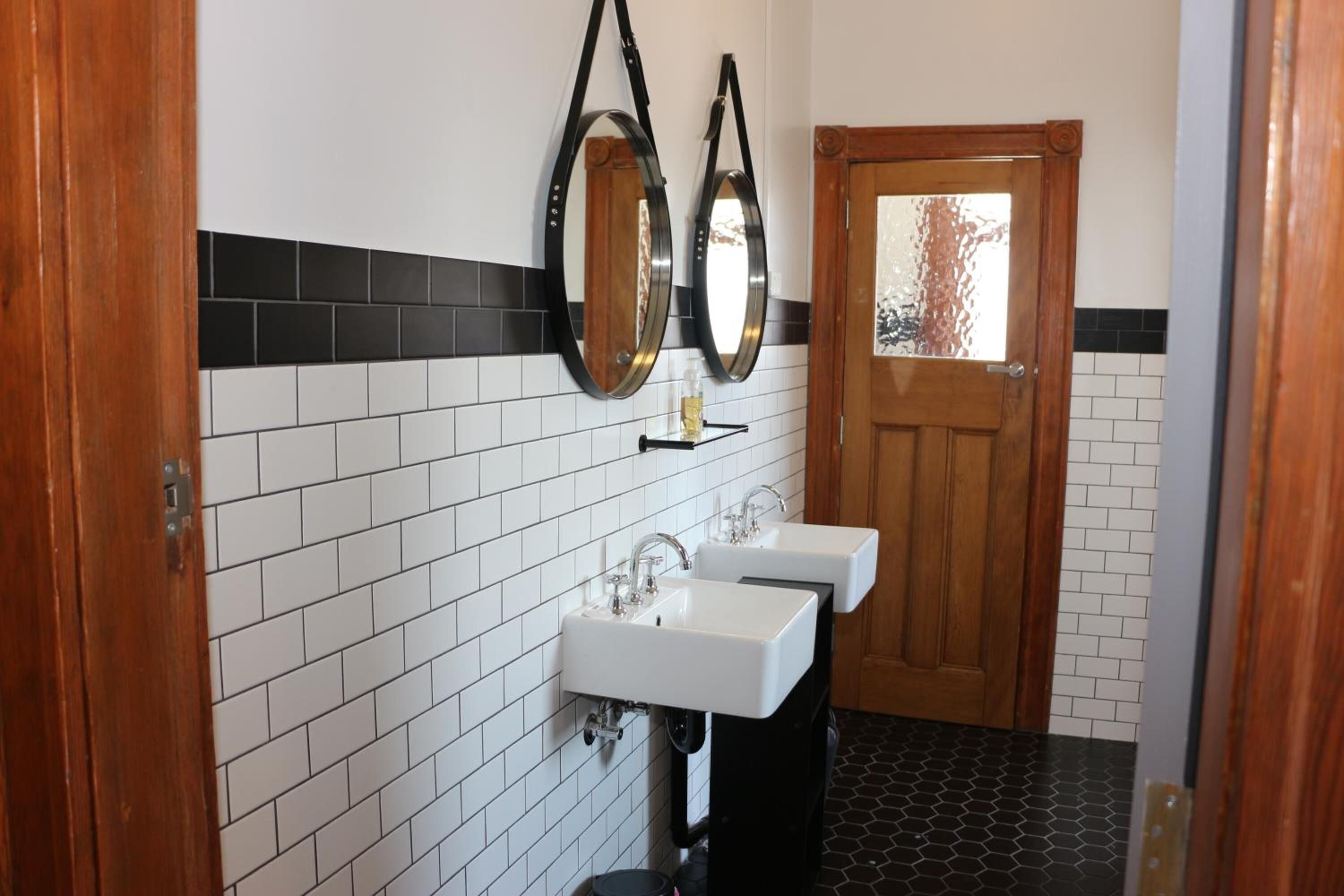 Un baño con dos lavamanos, una puerta de madera y un espejo con marco negro.