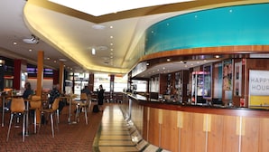 A curved reception desk with a sign that reads "HAPPY HOUR" in a hotel lobby with a patterned carpet and a high ceiling. - Guildford Hotel (Guildford)