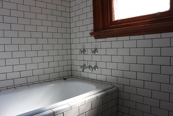 Un baño con azulejos blancos tipo metro, una bañera blanca y dos llaves.