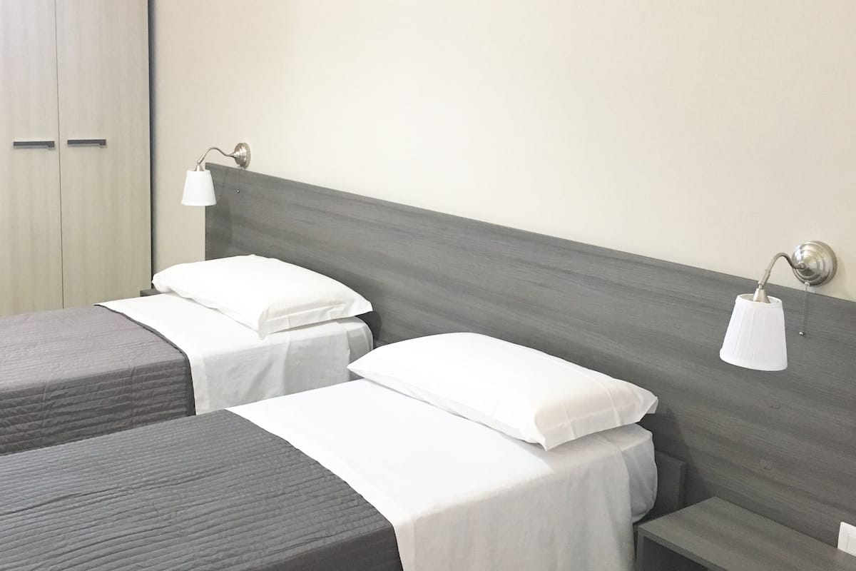 Quarto de hotel com duas camas, um guarda-roupa e uma mesa de cabeceira.