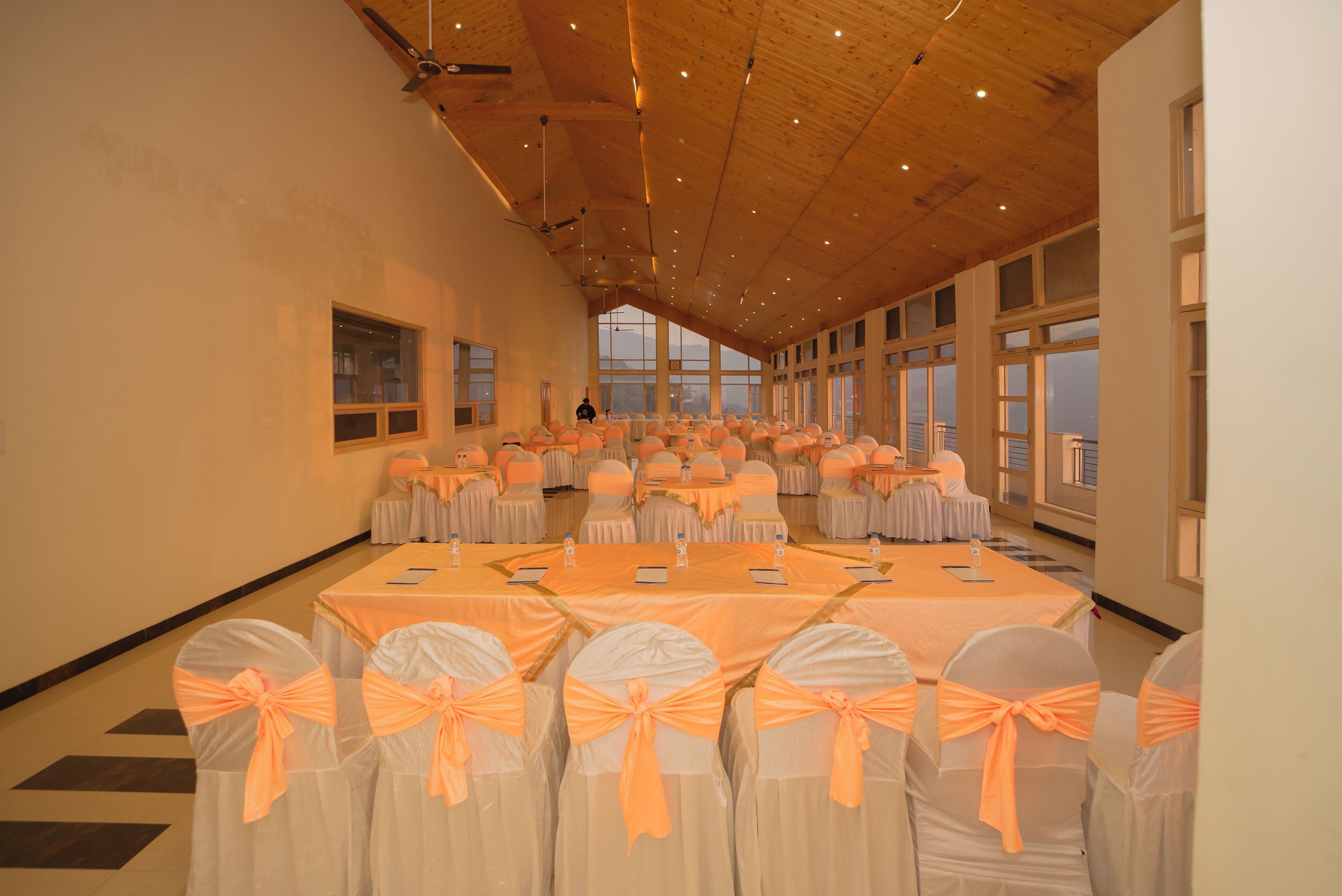 Une grande salle avec des rangées de tables et de chaises, chacune décorée de blanc et d’orange.