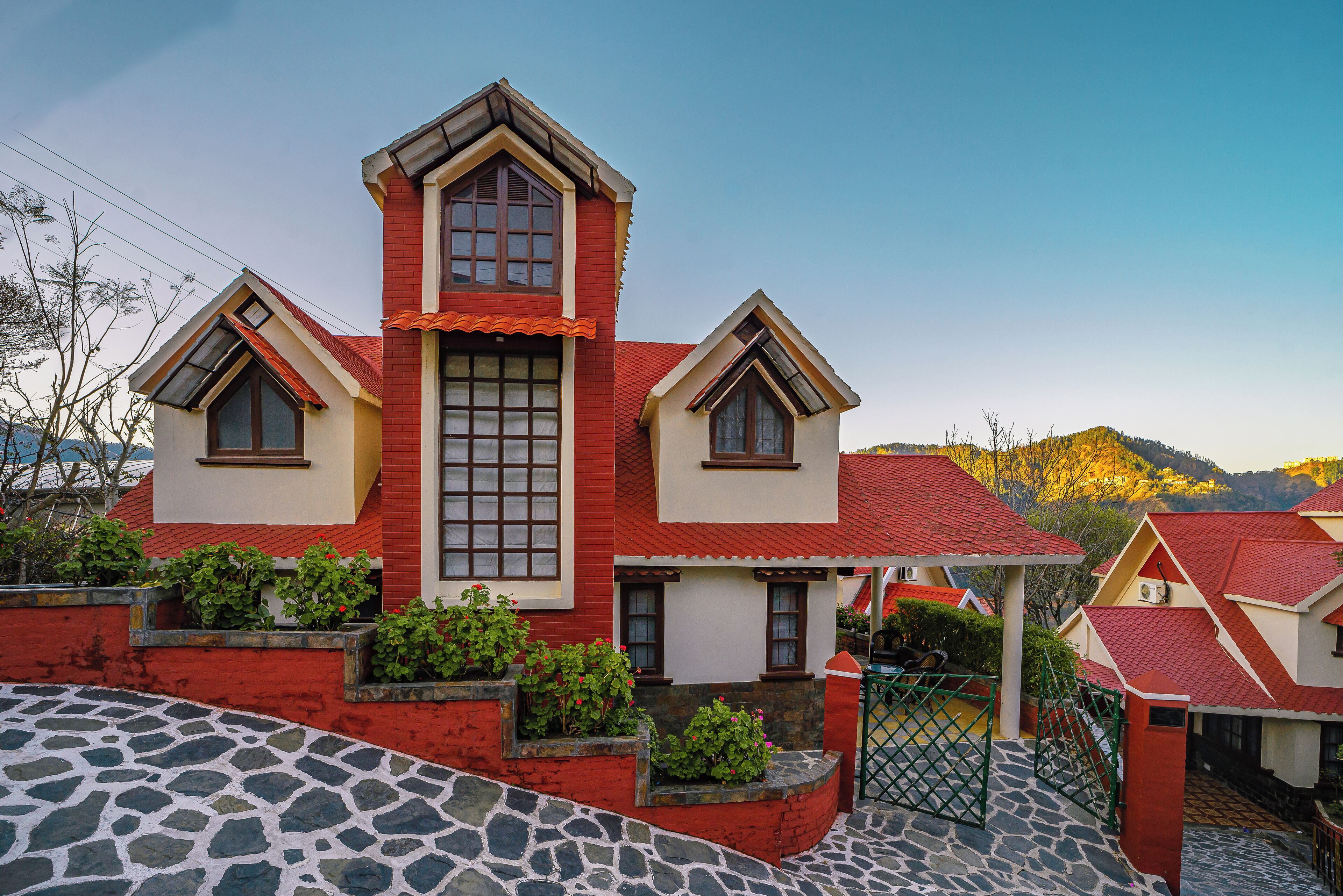 A two-story house with a red and white exterior, a stone-paved driveway, and a green gate.