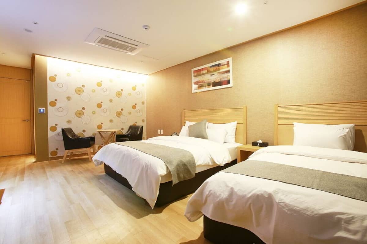 A hotel room with two beds, a desk, a chair, and a wall with a circular pattern.