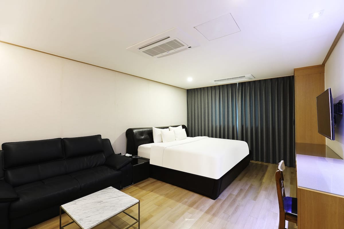 A hotel room with a bed, a black leather sofa, a small table, and a TV mounted on the wall.