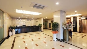 A hotel reception area with a reception desk, a clock, and a large potted plant. - Paju Golden Hill (Paju)