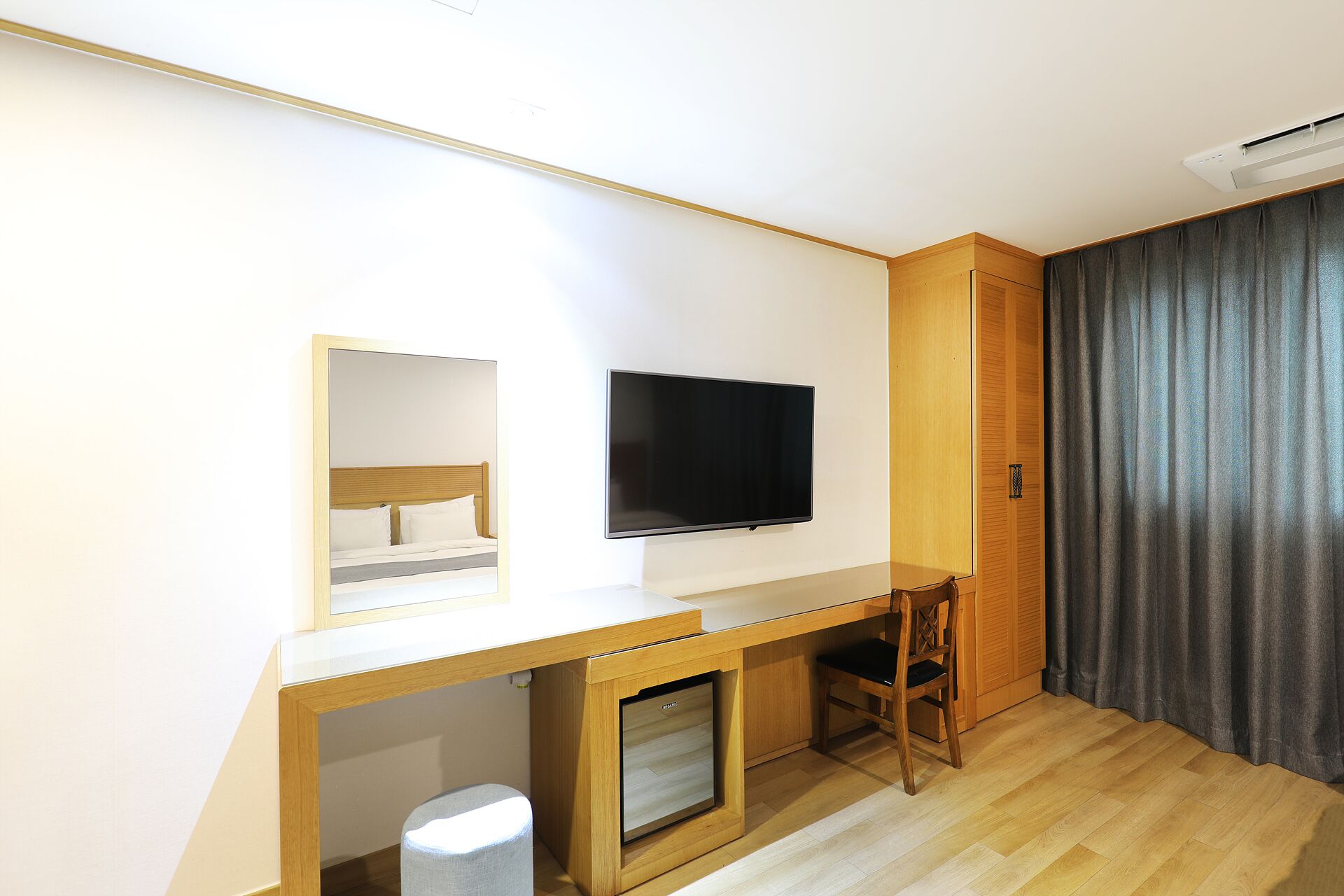 A compact room with a bed, a TV, a desk, a chair, and a small refrigerator.
