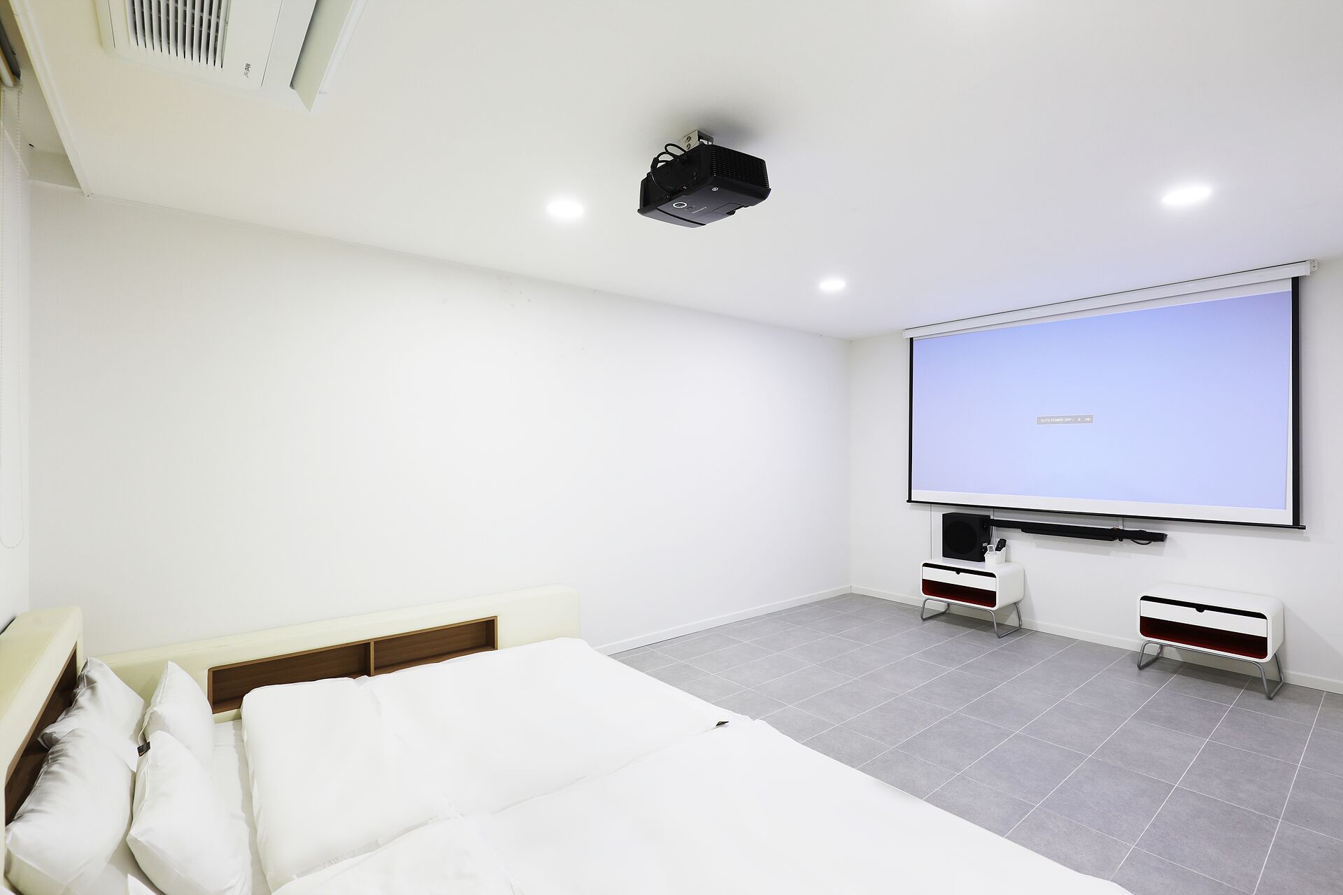 A modern hotel room with a large bed, a projector screen, and a flat-screen TV.