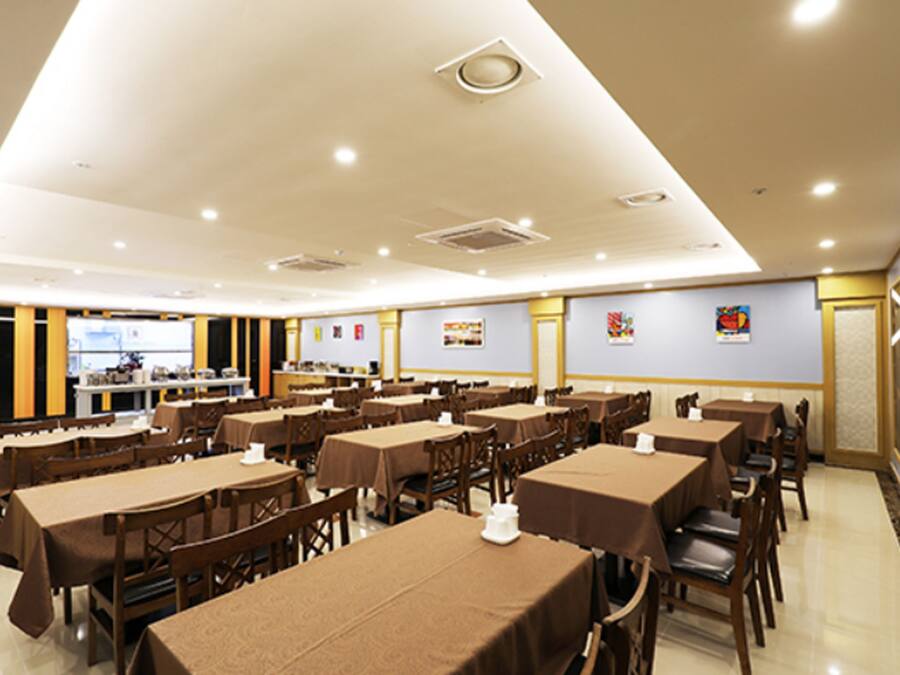 A spacious dining area with multiple tables and chairs, a kitchen in the background, and a mural on the wall.