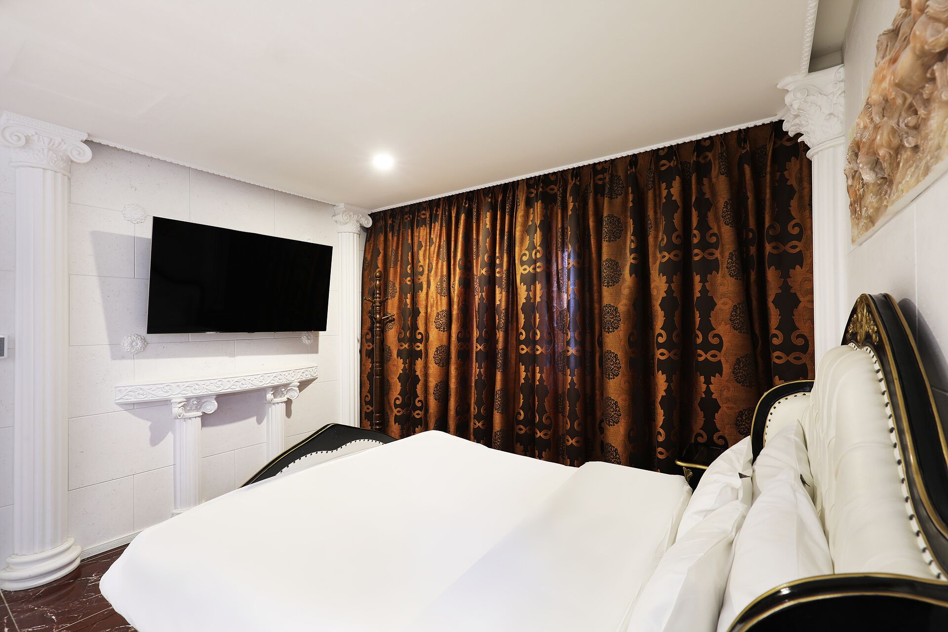 Habitación de hotel con cama, televisor de pantalla plana en la pared y un ventanal con cortinas.