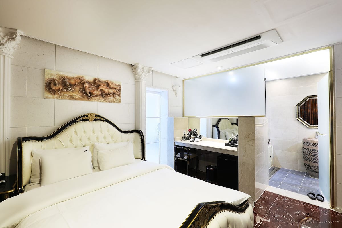 A hotel room with a large bed, a vanity with a mirror, and a bathroom with a shower and toilet.