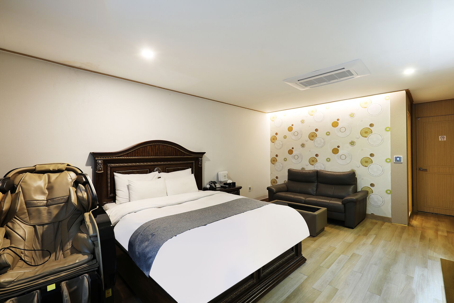 Habitación de hotel con cama, sillón de masaje, una mesita y pared con diseño circular.