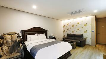 Habitación de hotel con cama, sillón de masaje, una mesita y pared con diseño circular.