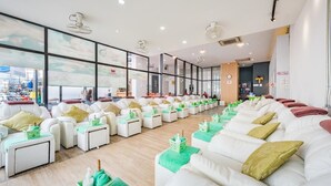 Een modern wellnesscentrum met rijen witte banken en groene kussens, grote ramen en uitzicht op de stad.