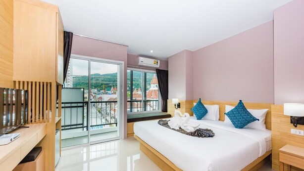 Een moderne hotelkamer met een groot bed, een bureau, een televisie en een balkon met uitzicht op gebouwen.