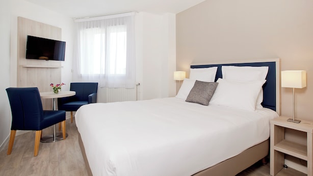 Une chambre d’hôtel comprenant un lit, un bureau avec deux chaises, un téléviseur fixé au mur et une fenêtre avec des rideaux.