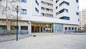Un bâtiment moderne doté d’une entrée en verre, d’une cour pavée et d’un lampadaire.