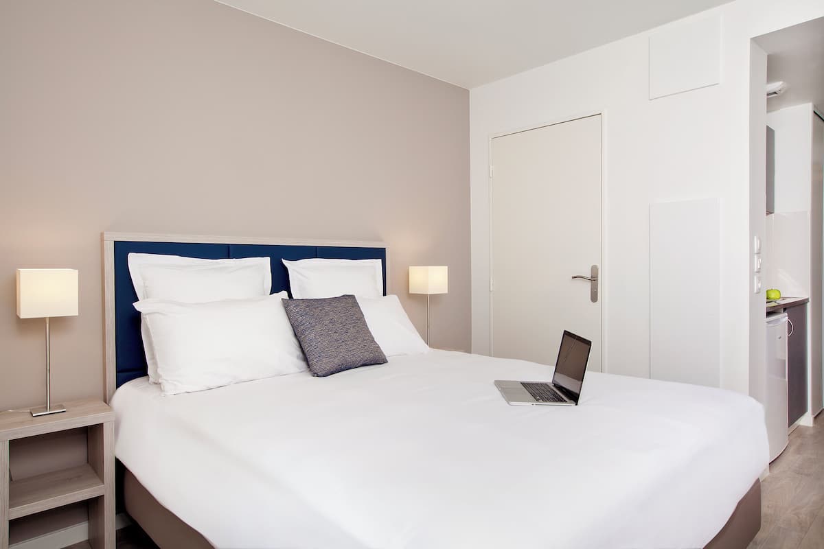 Un lit bien fait, avec un ordinateur portable, une lampe de chevet et une table de nuit.