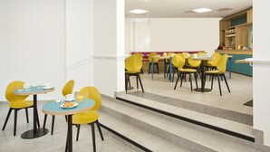 Un espace repas moderne avec des chaises et des tables jaunes, un escalier et un comptoir où sont exposés divers objets.