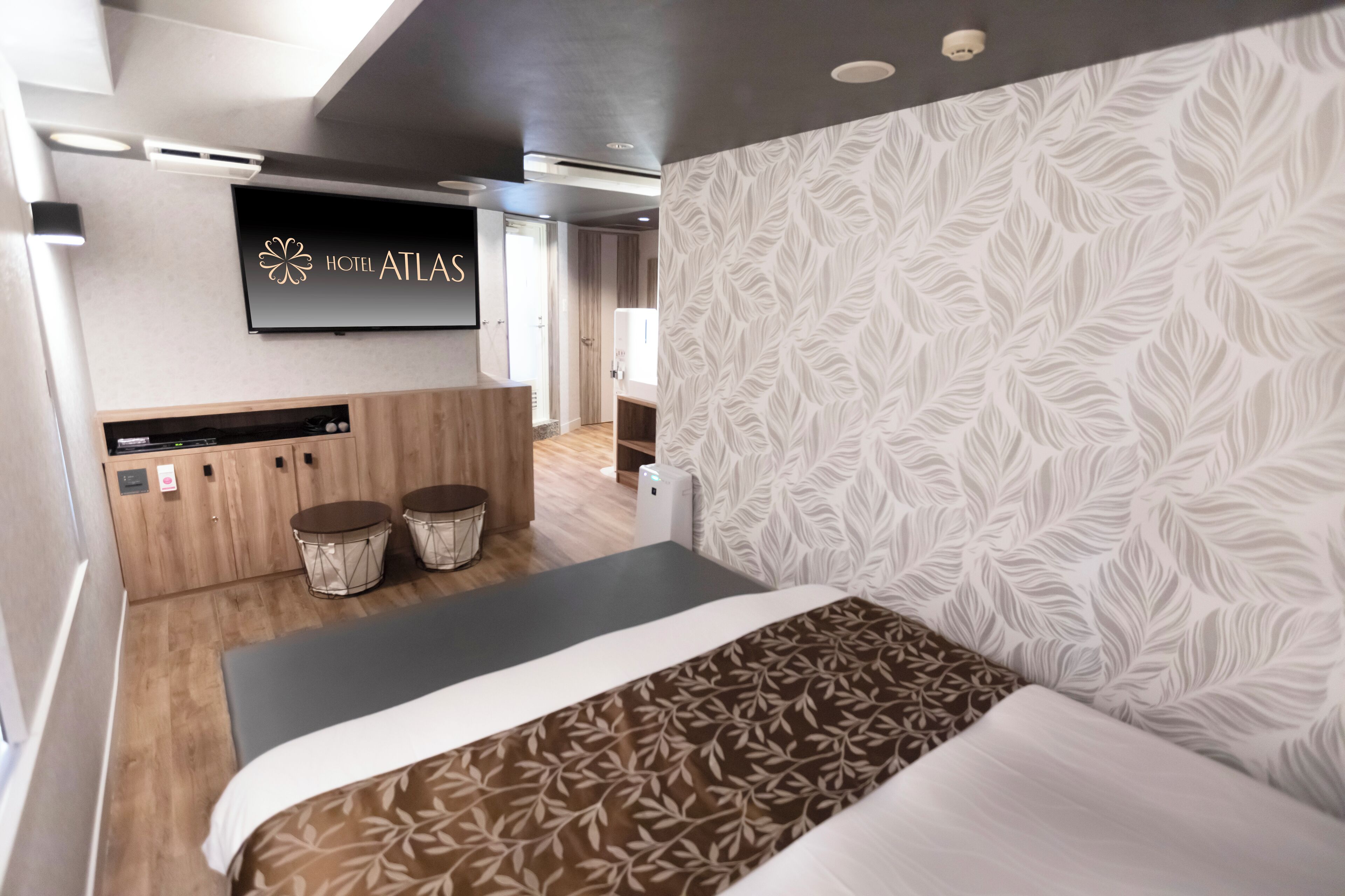 A modern hotel room with a bed, a desk, and a television displaying the hotel name.