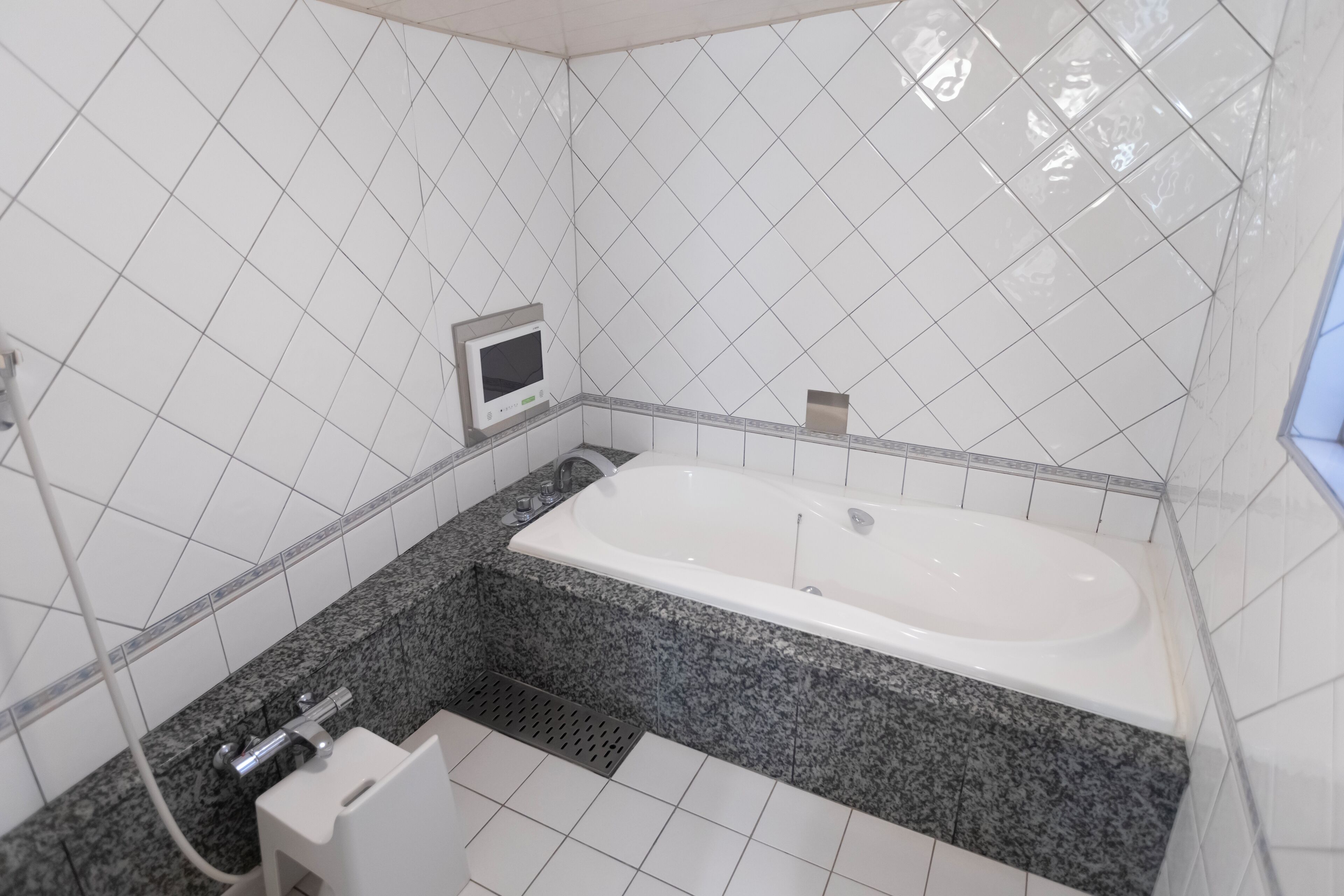 Un baño moderno con una bañera independiente, paredes de azulejos blancos y una encimera de granito.