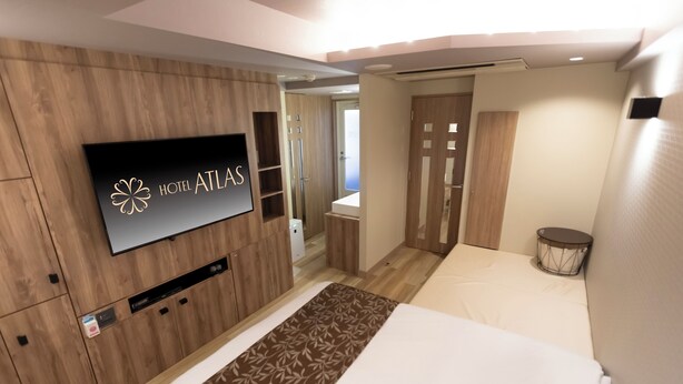 Quarto de hotel moderno com televisão de tela plana fixada em parede de madeira, cama com corredor estampado e uma pequena mesa redonda.