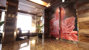 Um hall de entrada com balcão de recepção, área de estar, plantas em vasos e um grande mural floral na parede.