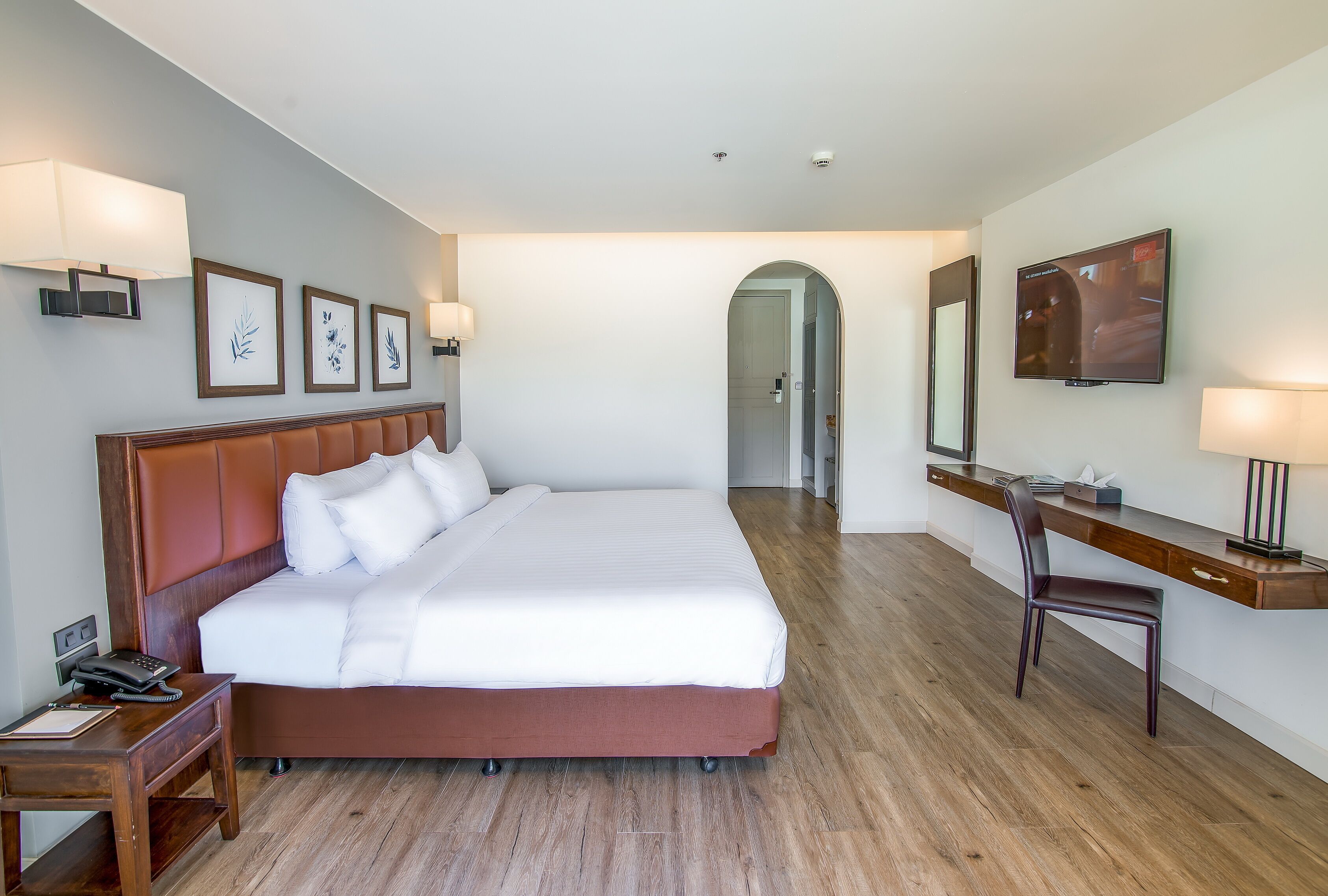 Habitación de hotel con una cama grande, un escritorio con una silla, un televisor y cuadros en la pared.