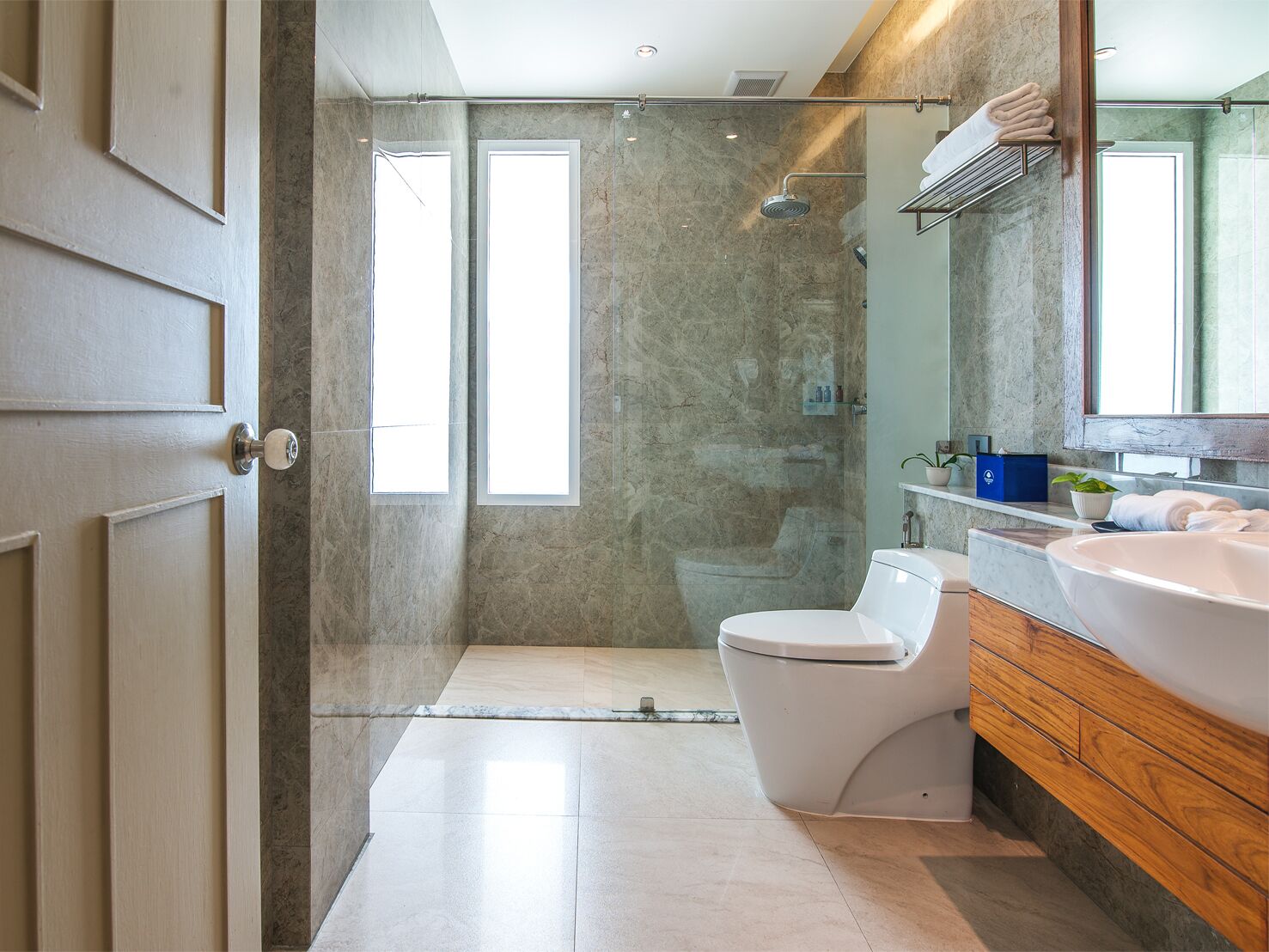 Un baño moderno con ducha de vidrio, inodoro blanco y tocador de madera con un lavamanos grande.