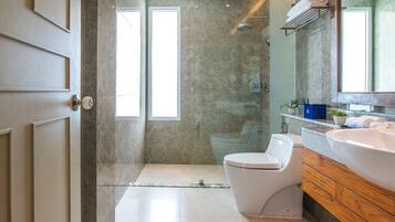 Un baño moderno con ducha de vidrio, inodoro blanco y tocador de madera con un lavamanos grande.