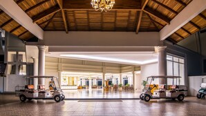 A spacious lobby with a high wooden ceiling and a chandelier, featuring two golf carts and a reception area in the background.