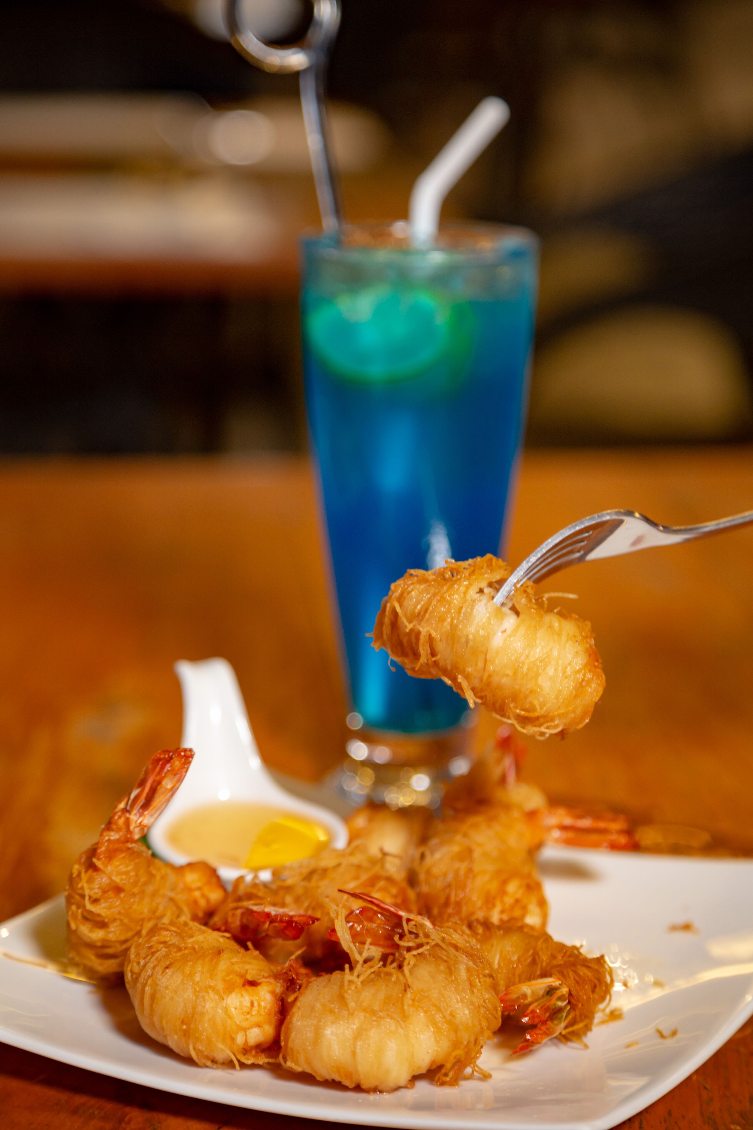 A plate of fried shrimp with a dipping sauce and a glass of blue beverage with a straw.