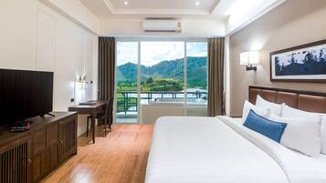 A hotel room with a large bed, a TV, a desk, and a balcony with a scenic view.
