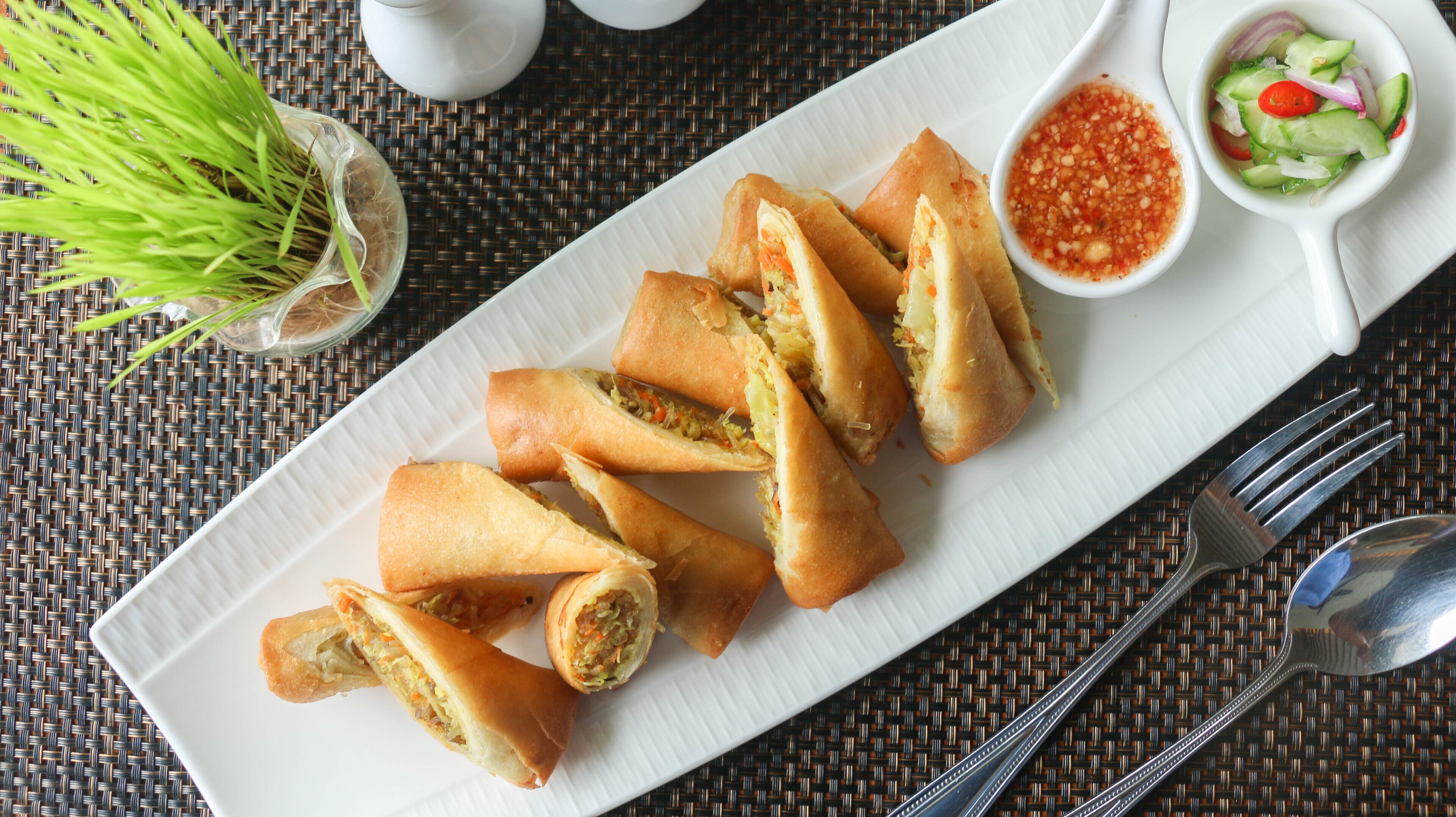 A plate of spring rolls with a side of dipping sauce and salad.
