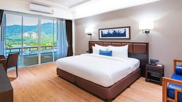 A hotel room with a large bed, a desk, and a chair. There is a balcony with a view of the mountains.