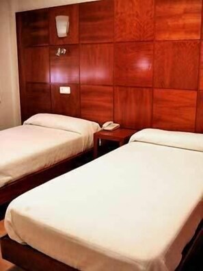 A hotel room with two single beds, a wooden headboard, a bedside table with a phone, and a wall-mounted light. - Hotel Trefacio (Zamora)