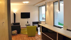 Un espacio de oficina moderno con un televisor de pantalla plana montado en la pared, un mostrador de recepción y una zona de estar con una silla amarilla.