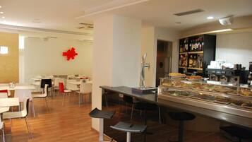 A modern cafeteria with a central serving station, multiple seating areas, and a variety of food options displayed.