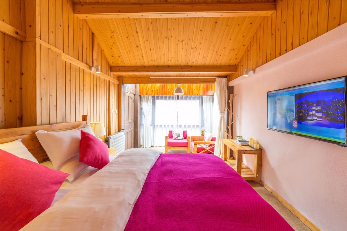 Una habitación de cabaña de madera con una cama, un escritorio y un televisor en la pared.