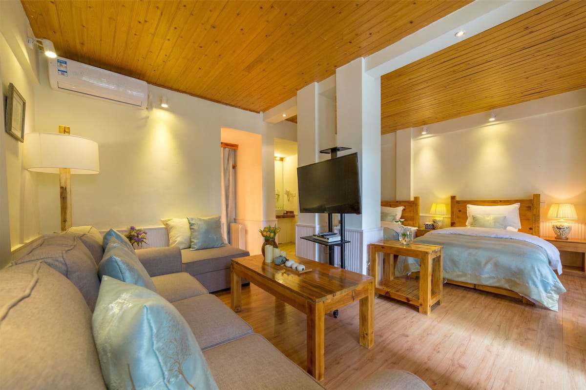 Una habitación de hotel moderna con techo de madera, un sofá, una cama, un televisor y una pequeña mesa con lámpara.