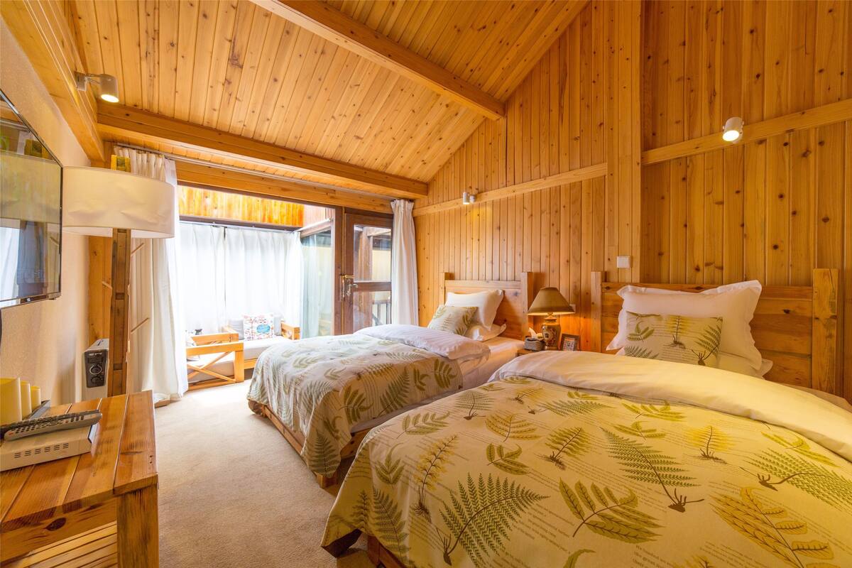 Una habitación de cabaña de madera con dos camas, un banco de madera, una mesa y un televisor.